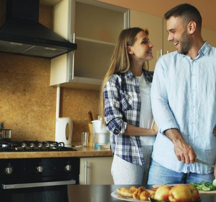 Happy young couple embracing and talking in the kitchen while cooking breakfast at home in the morning