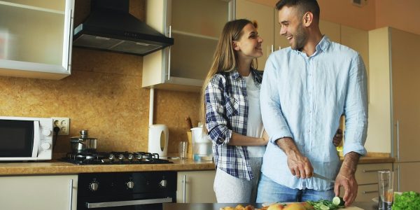 Happy young couple embracing and talking in the kitchen while cooking breakfast at home in the morning