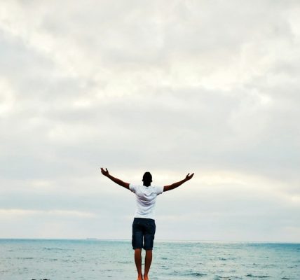 man raising hands standing near seashore during daytime